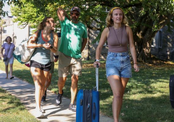 A dad and two students carrying bags as they move into the dorms