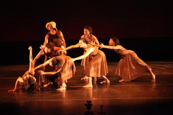 Seven dancers on a stage in golden light