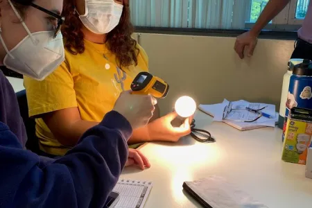 Two students use a device to measure lumens emited by an LED lightbulb in a classroom
