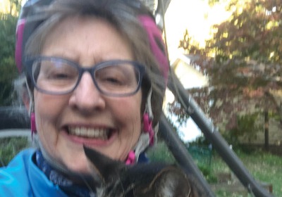 Portrait of Susan Burt wearing a bike helmet and holding a tabby cat.