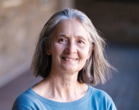 Kathy Tierney stands with arms crossed, smiling, wearing a blue shirt