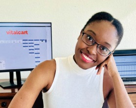 Portrait of Adaobi Kanu seated in front of a computer, the monitor displaying the Vitalcart extension