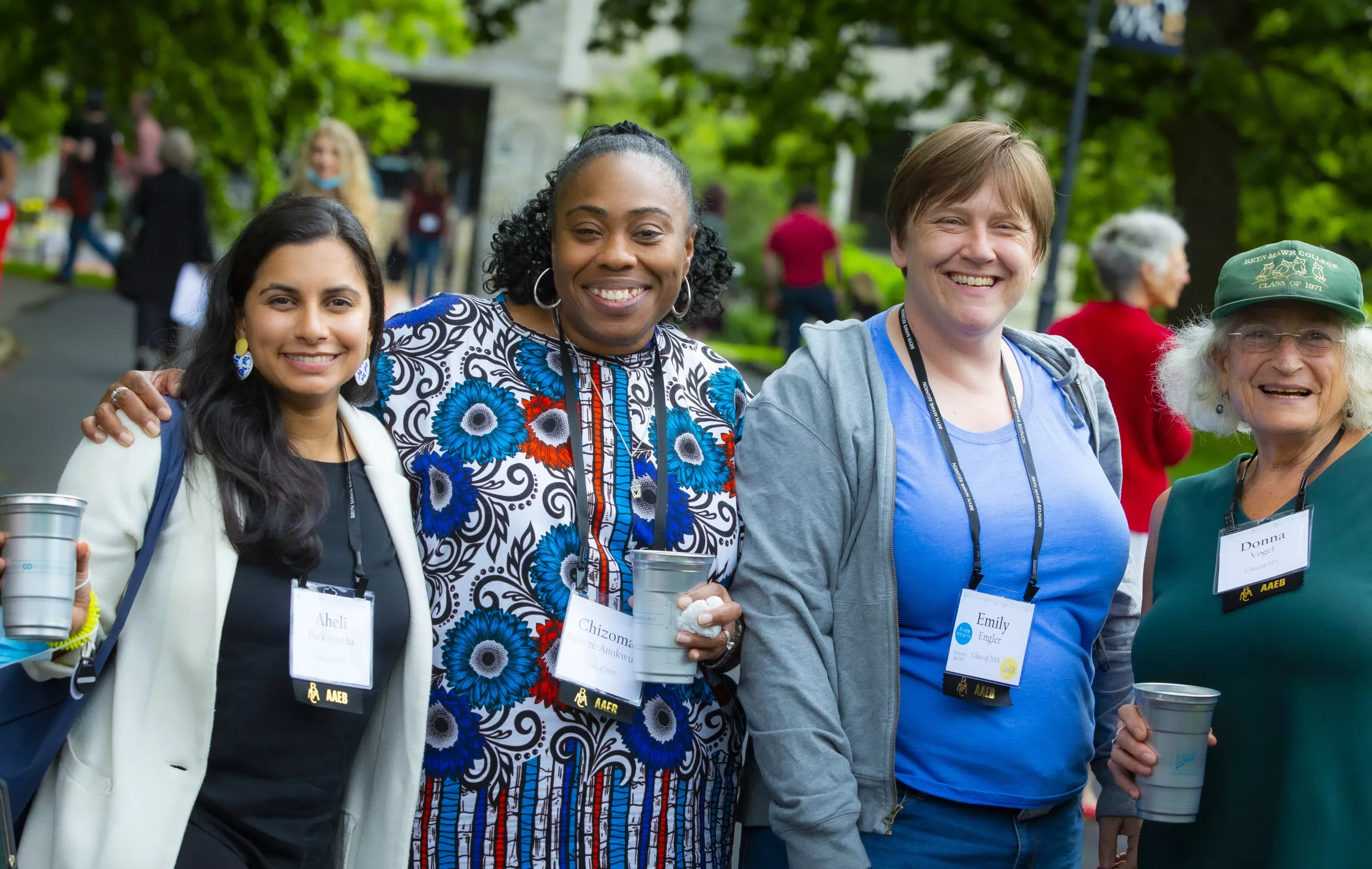 Four alums are outside, smiling at the camera and holding cups.