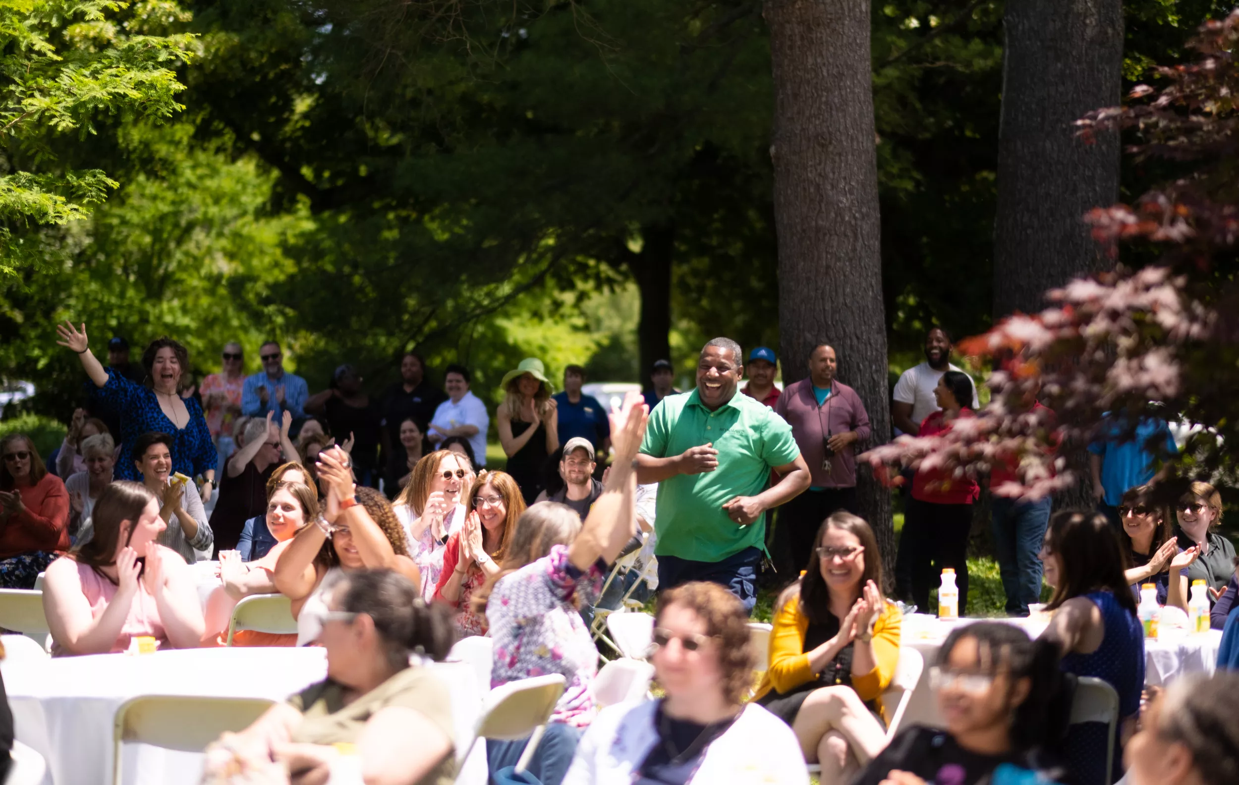 Man smiling and running through crowd of clapping people sitting at picnic tables