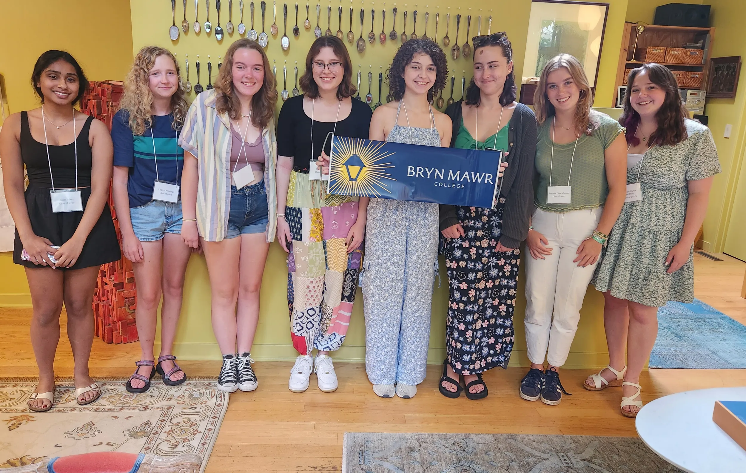 8 students smile at the camera. They are standing in front of a wall of decorative spoons.
