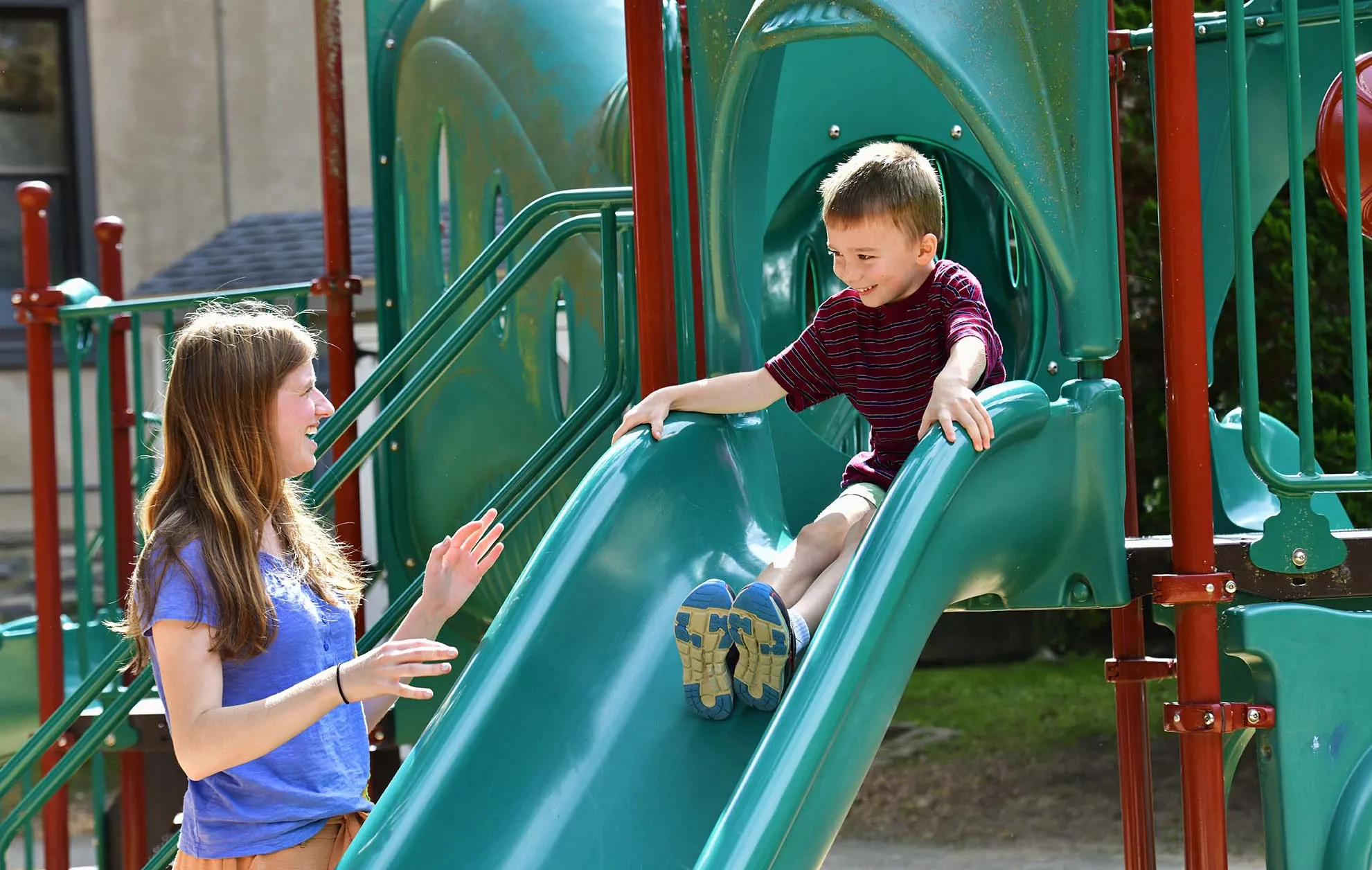 Child on playground slide with teacher
