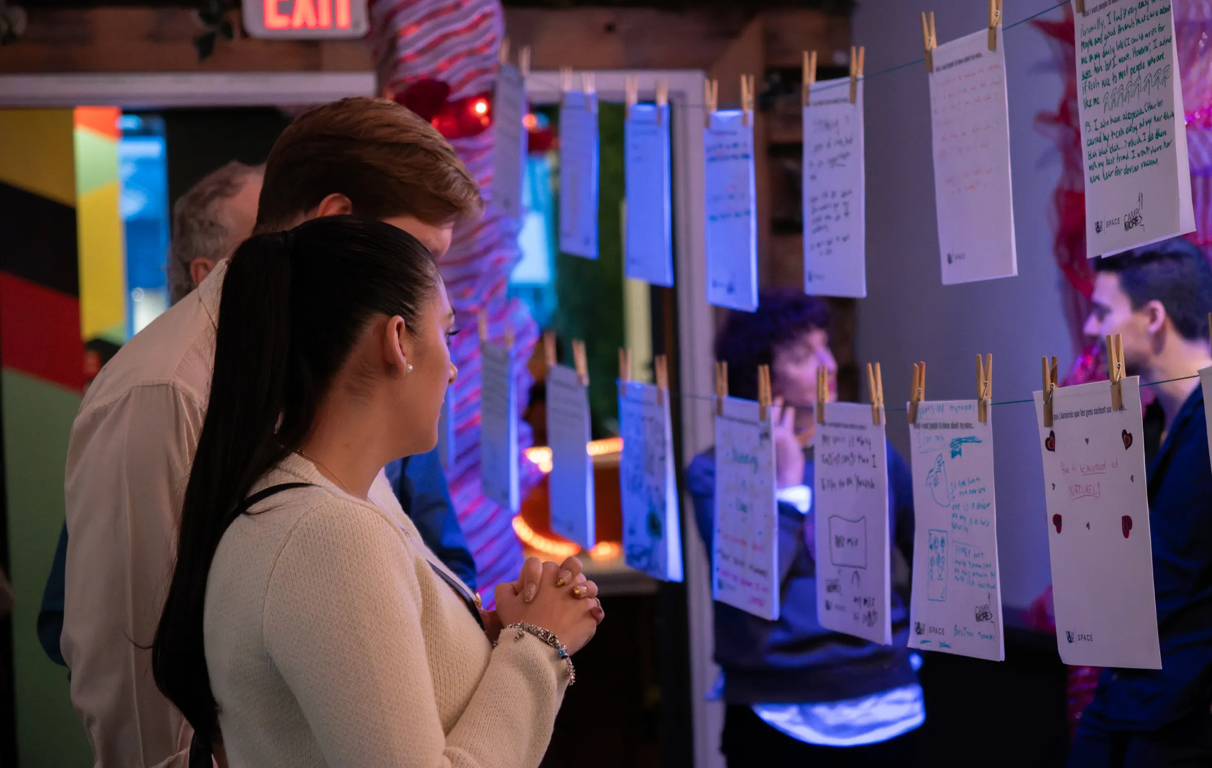 People look at pieces of paper hung on a clothes line. The papers have written reflections from people of all ages.