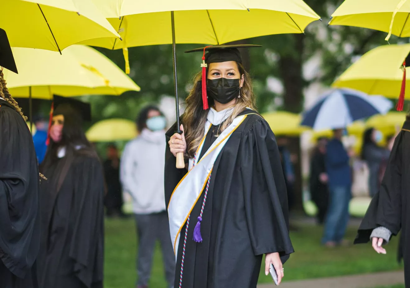 Students walk to graduation with yellow umbrellas