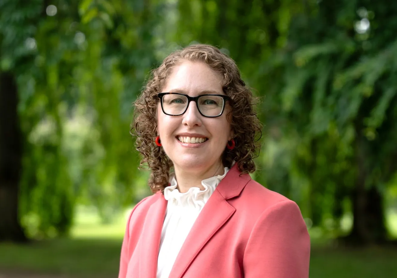 Woman in coral blazer in front of trees