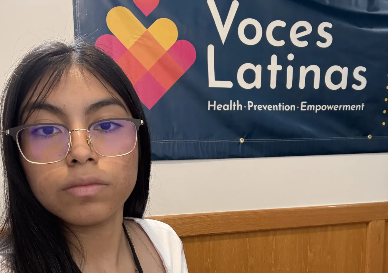 Kasey standing in front of a Voces Latinas sign