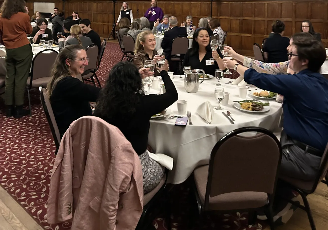 A group of alums sit at a round table in Great Hall, with their drinks raised in a toast