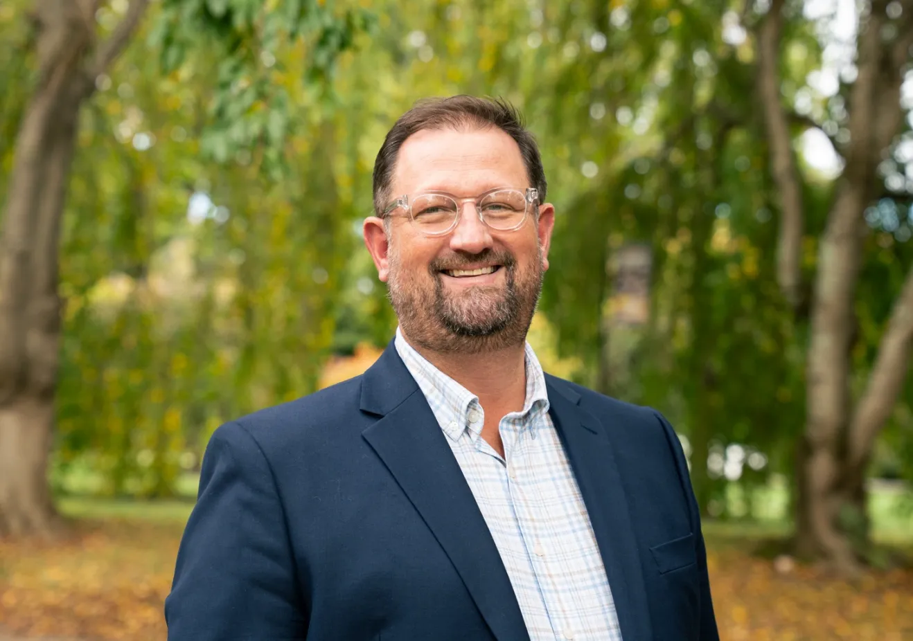 Man standing in front of trees with blue blazer and glasses