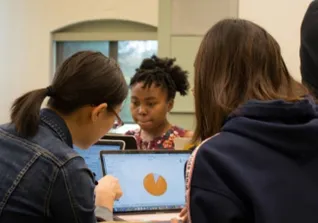 Three students standing closely look at computers