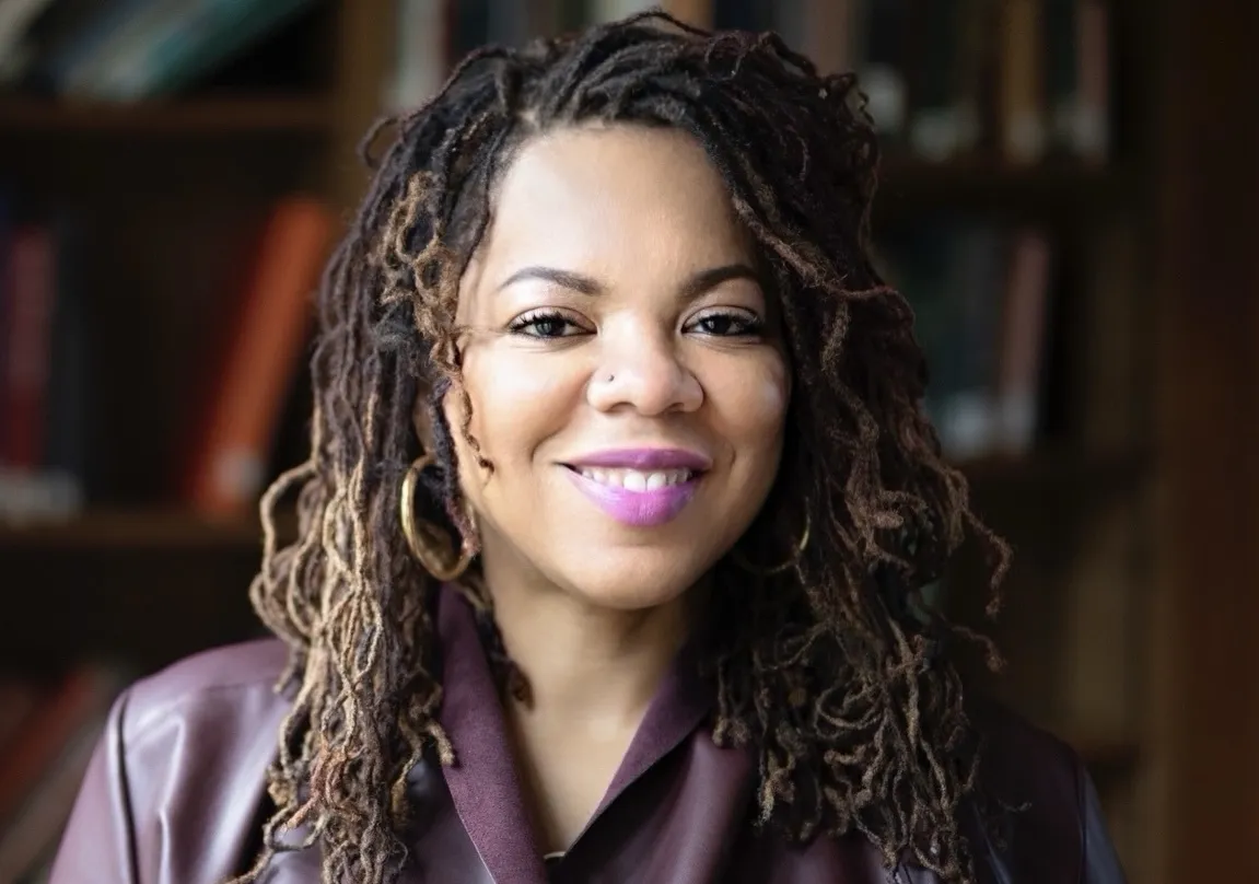 Woman facing camera with curly hair and brown jacket