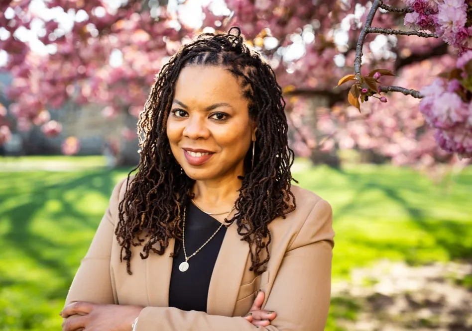 Woman in tan blazer standing in front of tree