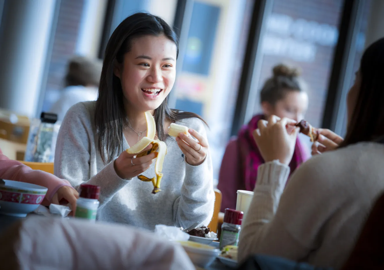A Bryn Mawr College student eats a banana while talking to a friend at New Dorm Dining Hall
