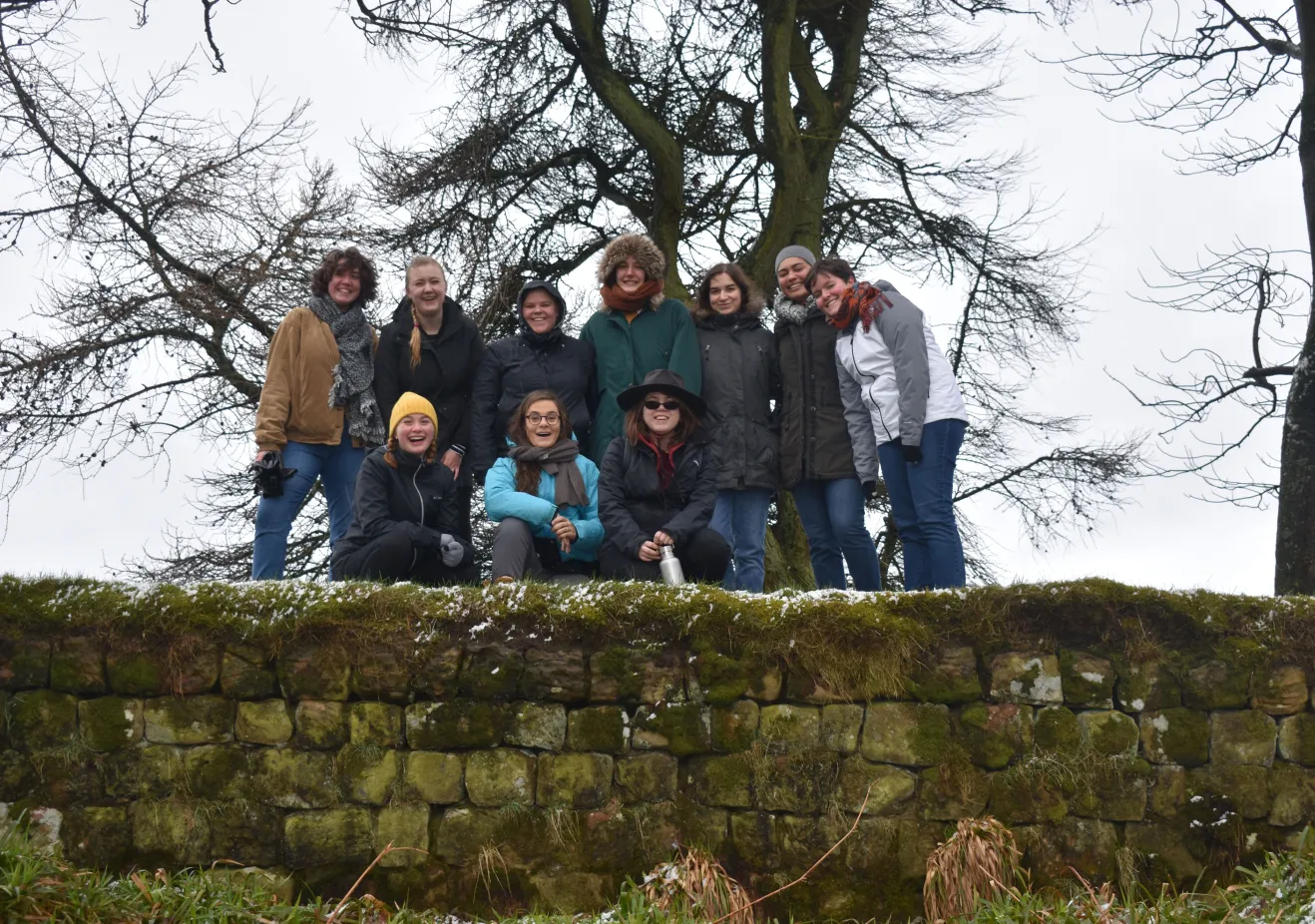 A group of Classical and Near Eastern Archaeology students stand on a green mossy portion of Hadrian's wall in winter