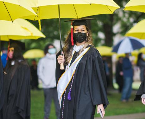 Students walk to graduation with yellow umbrellas