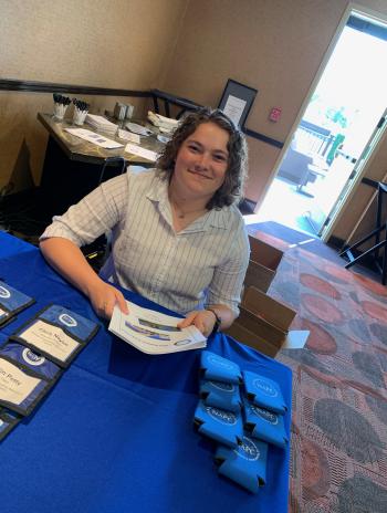 Emma Ryan sitting down at National Association for Prosecution Coordination conference volunteer table