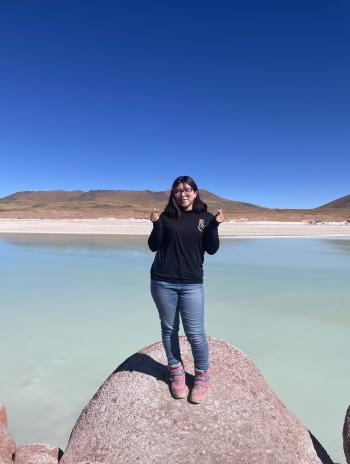Michelle Lamadrid Benavides standing in front of a lake making finger hearts. 