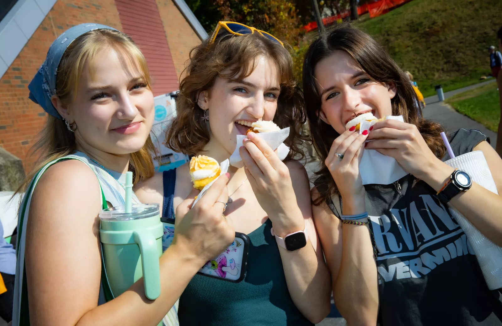 Three students eating cupcakes pose for the camera mid-bite