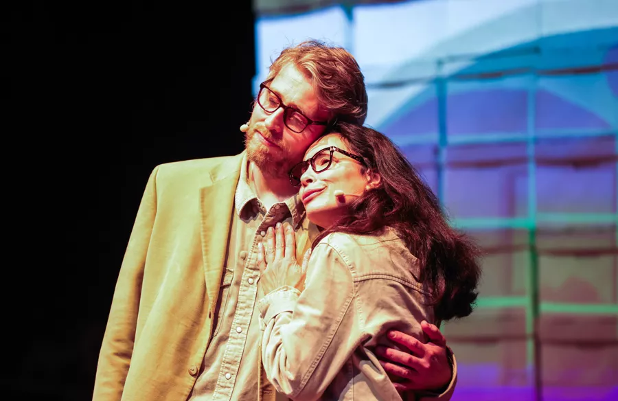 Two actors embrace in front of colorful screen