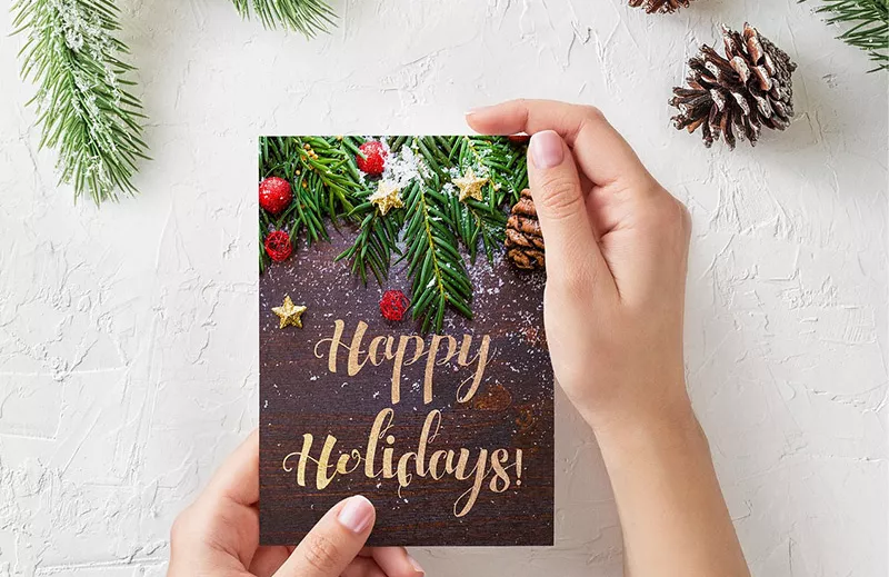 Hands holding a card that reads Happy Holidays