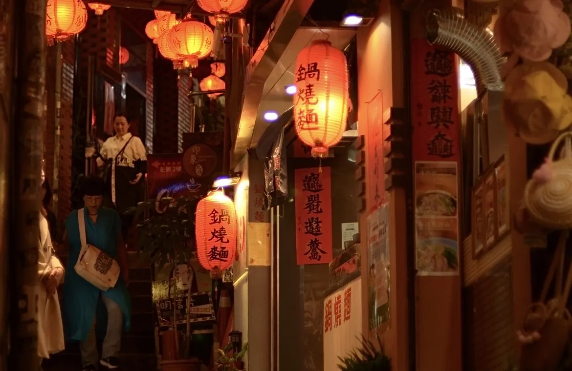 an image of a narrow street in Taiwan at night, lit by many warmly-colored lanterns