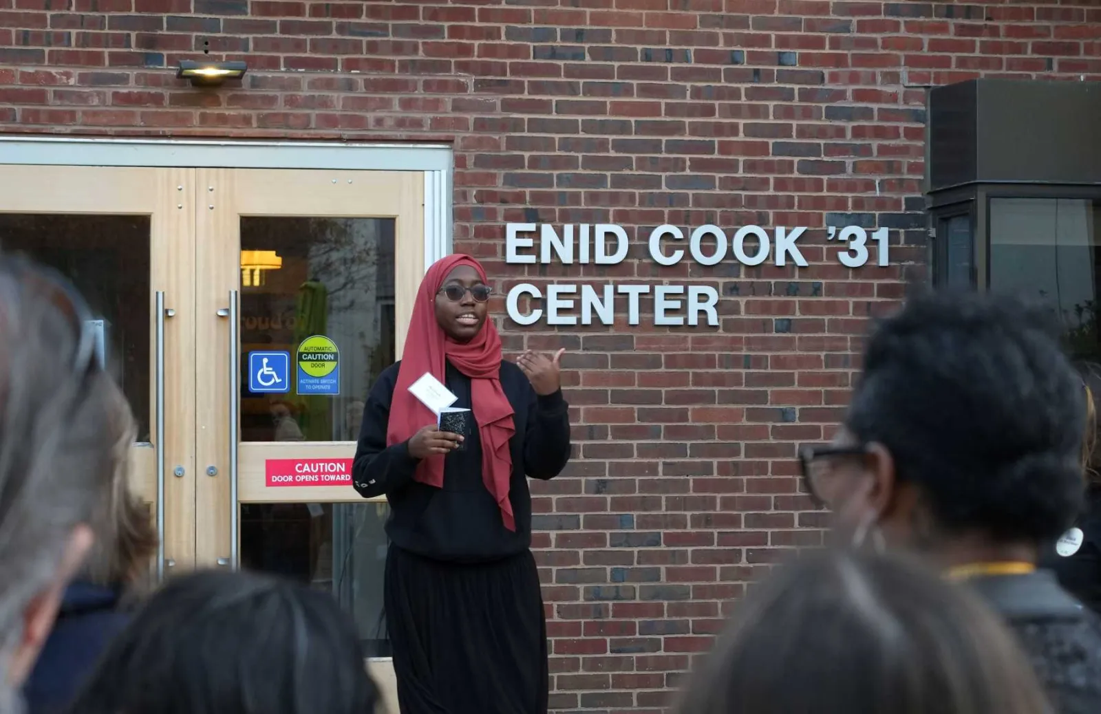 A student stands in front of the Enid Cook Center, talking to a crowd