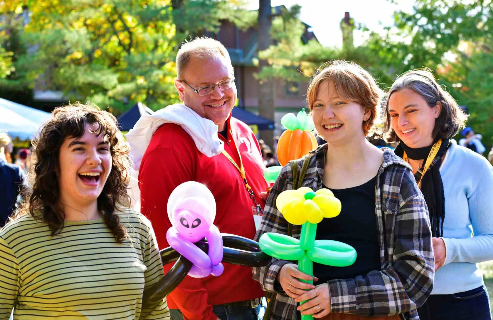 A group of people, standing outside, hold balloon animals and laugh.