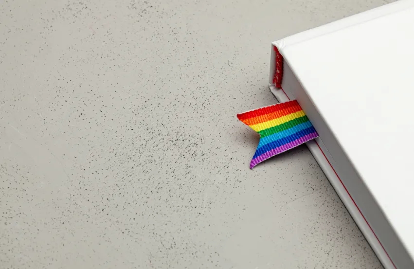 A white book, with a rainbow ribbon as a bookmark