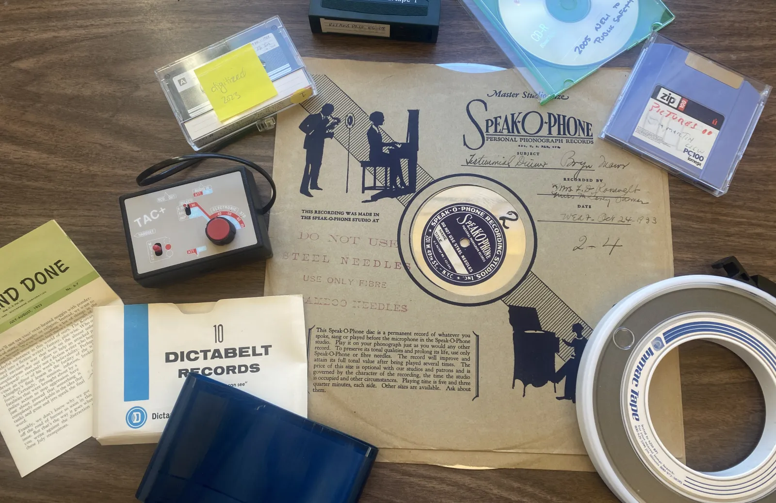 A record, CD, tape, floppy disk, and other assorted old or obsolete media types sitting on a desk.