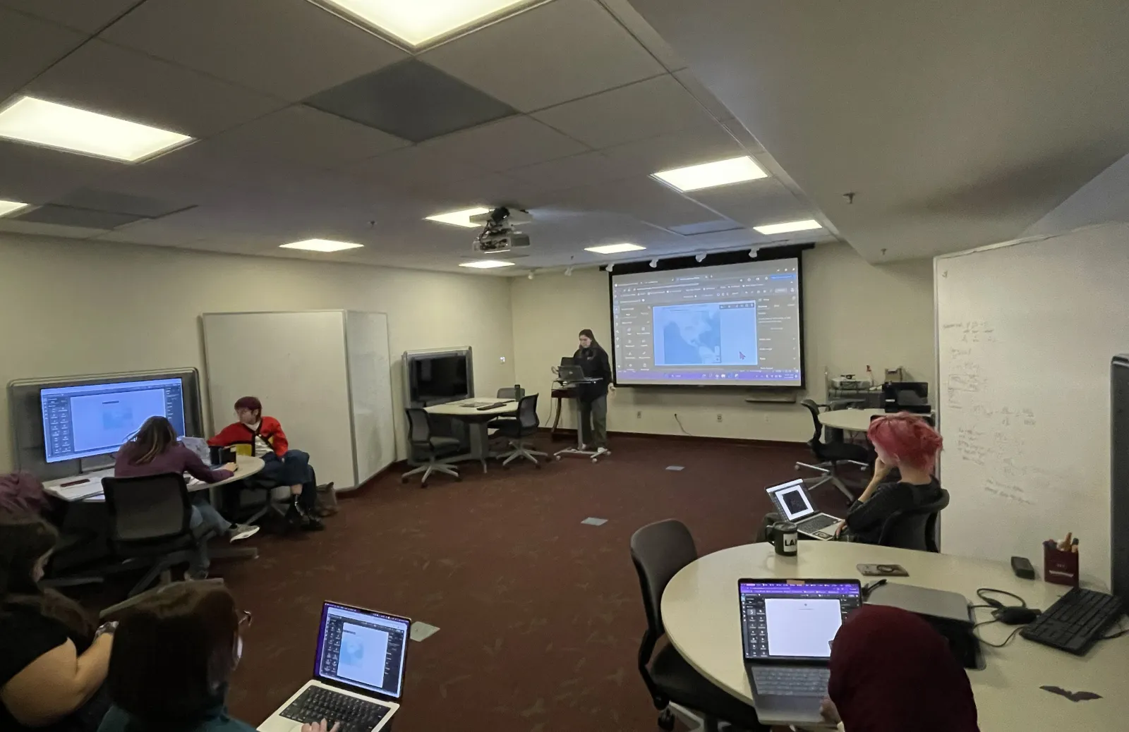 a presenter in the DMCL with people on laptops and a display board showing a map