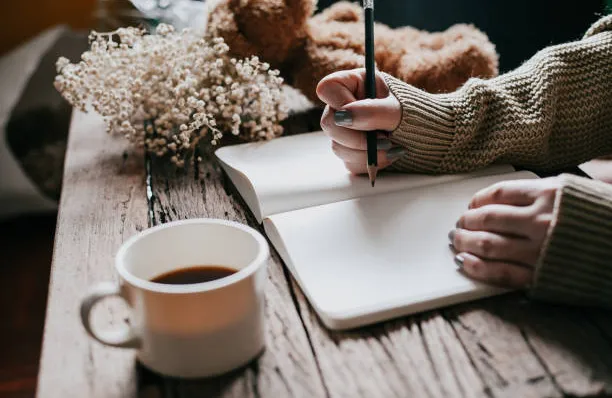 image shows a person working on a journal with a warm cup of tea