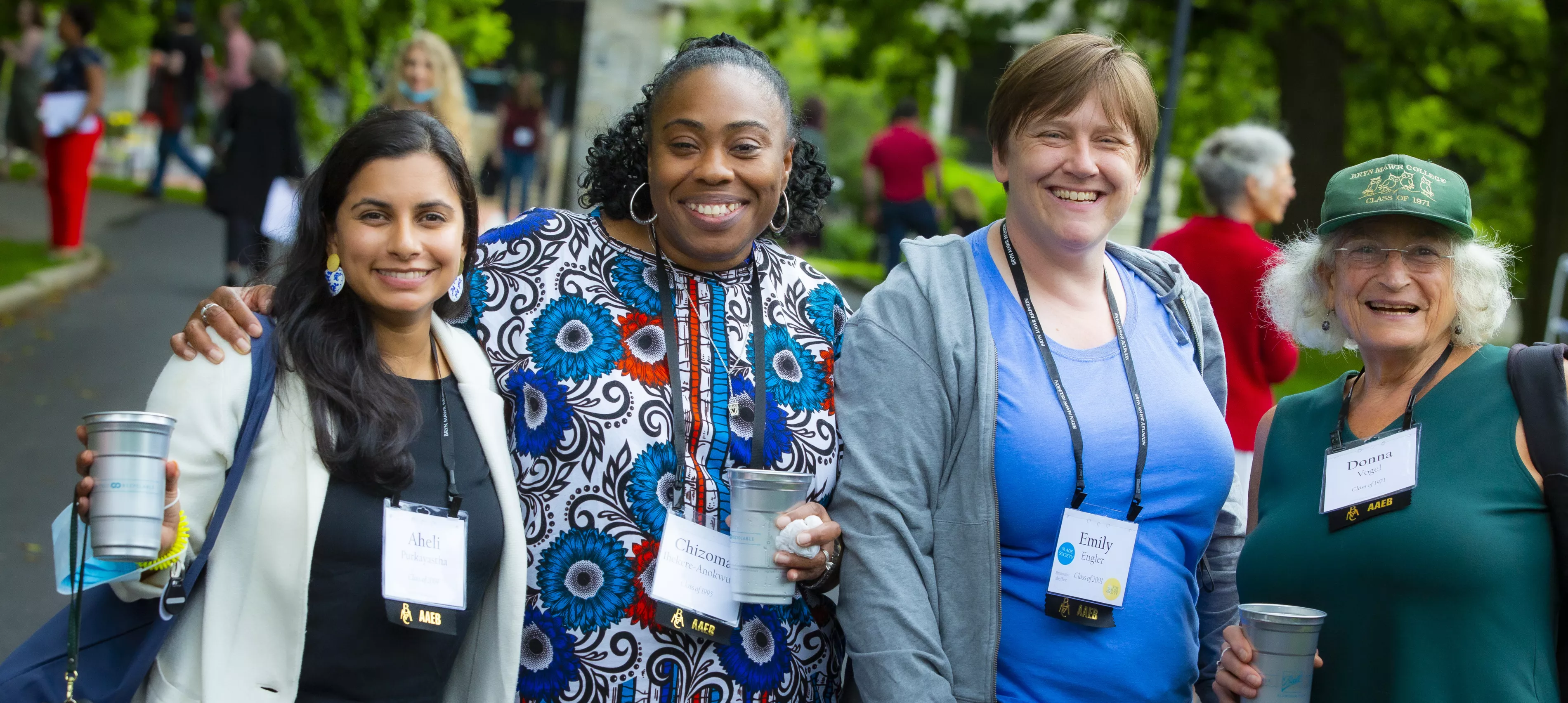Four alums are outside, smiling at the camera and holding cups.