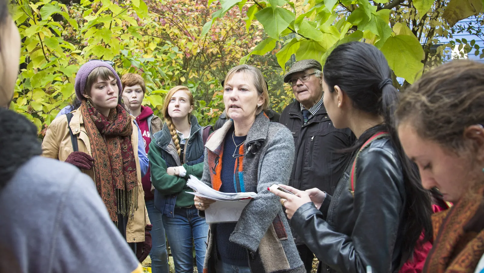 A group of Environmental Studies students listen to a professor talk in a forest
