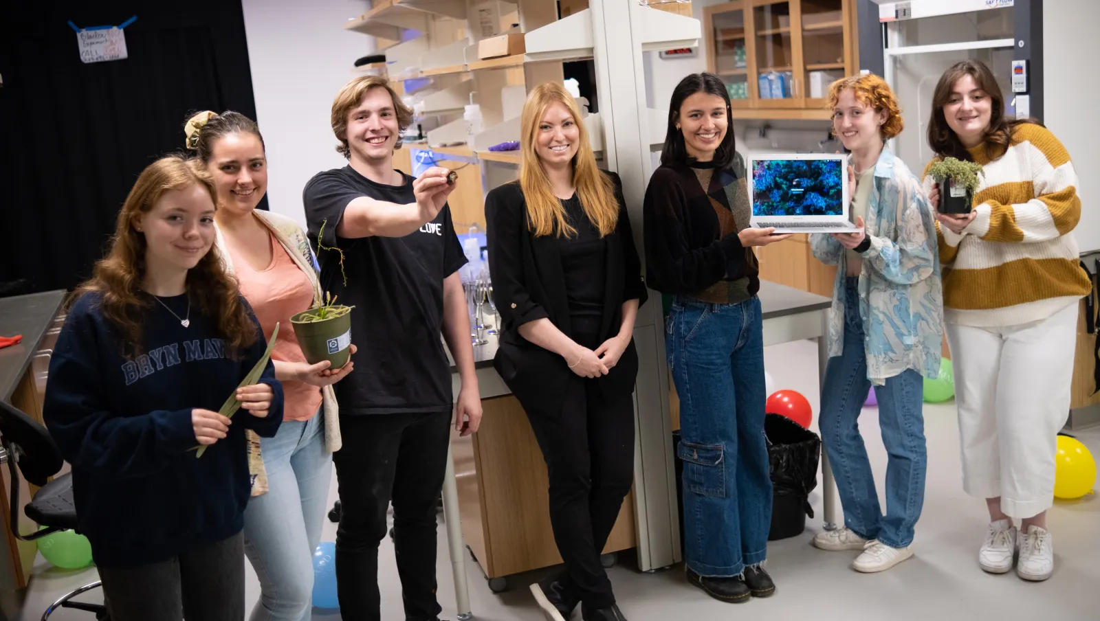 Seven physics students post with research materials at the biophysics lab opening