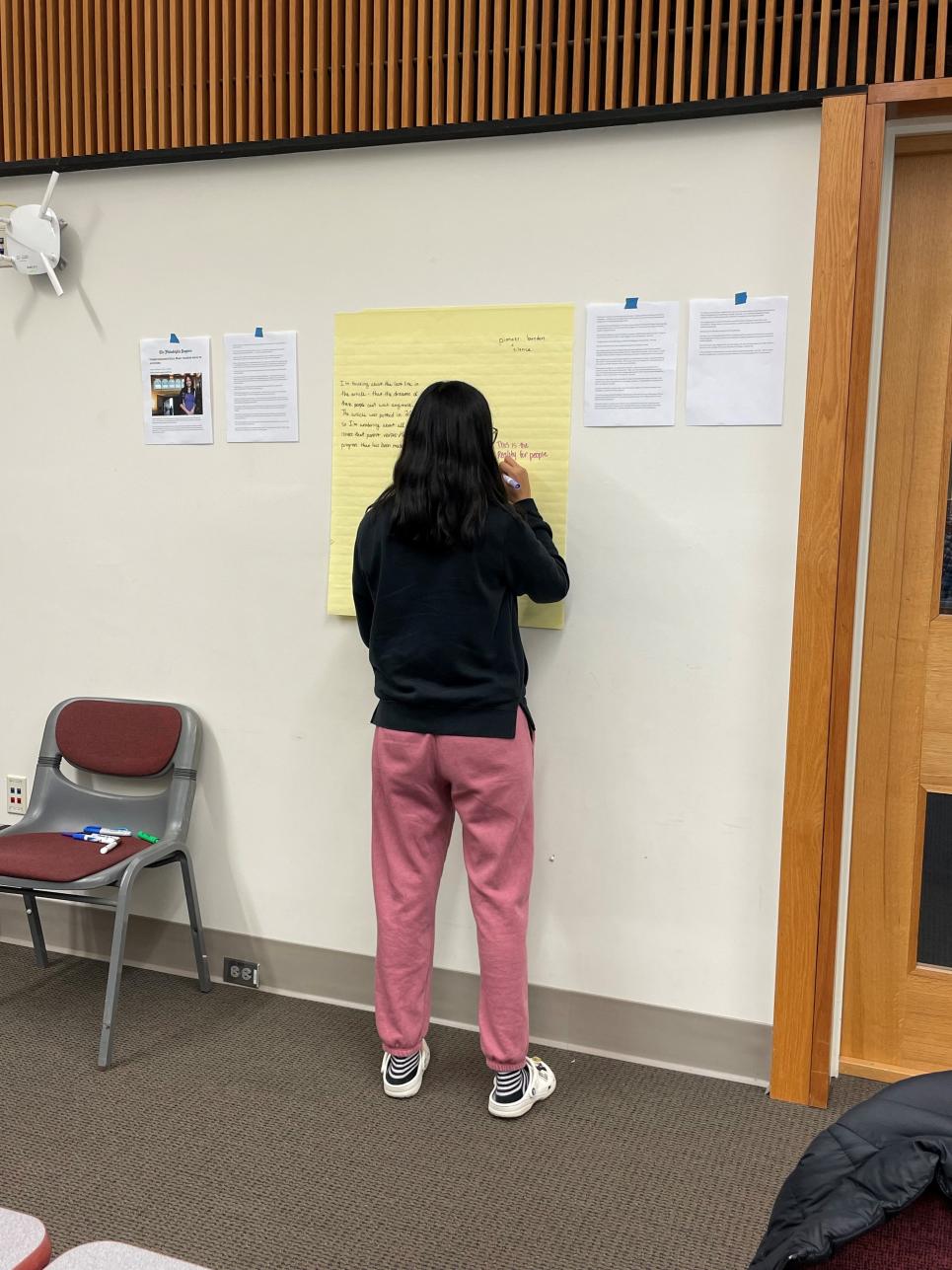 Student writing down thoughts to an article on a poster sticky note as part of gallery walk activity