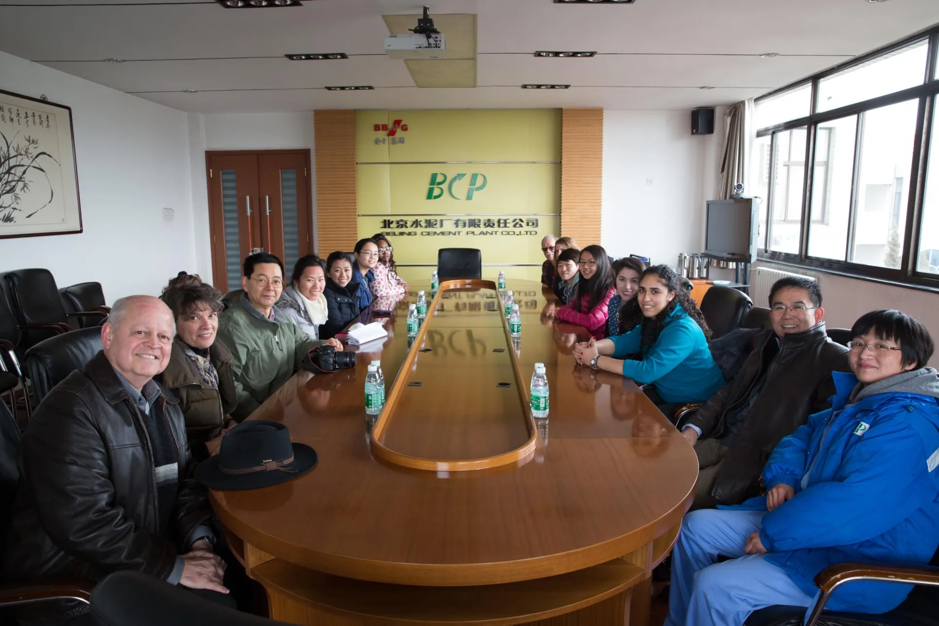 A group of students and professors sit around a boardroom table in China, facing the camera and smiling