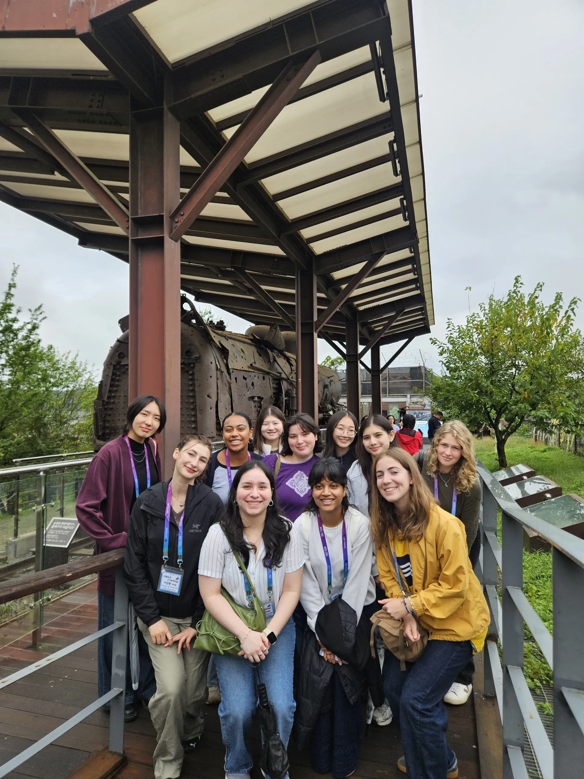 A group of students pose with a piece of equipment in the background in south korea