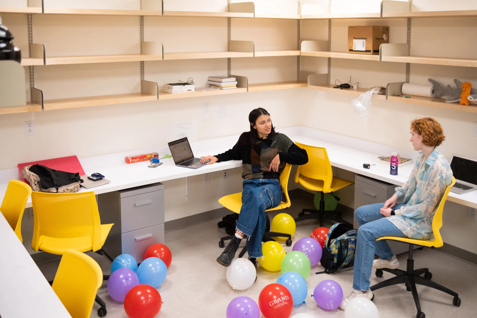 Two physics students talk in a workspace full of balloons