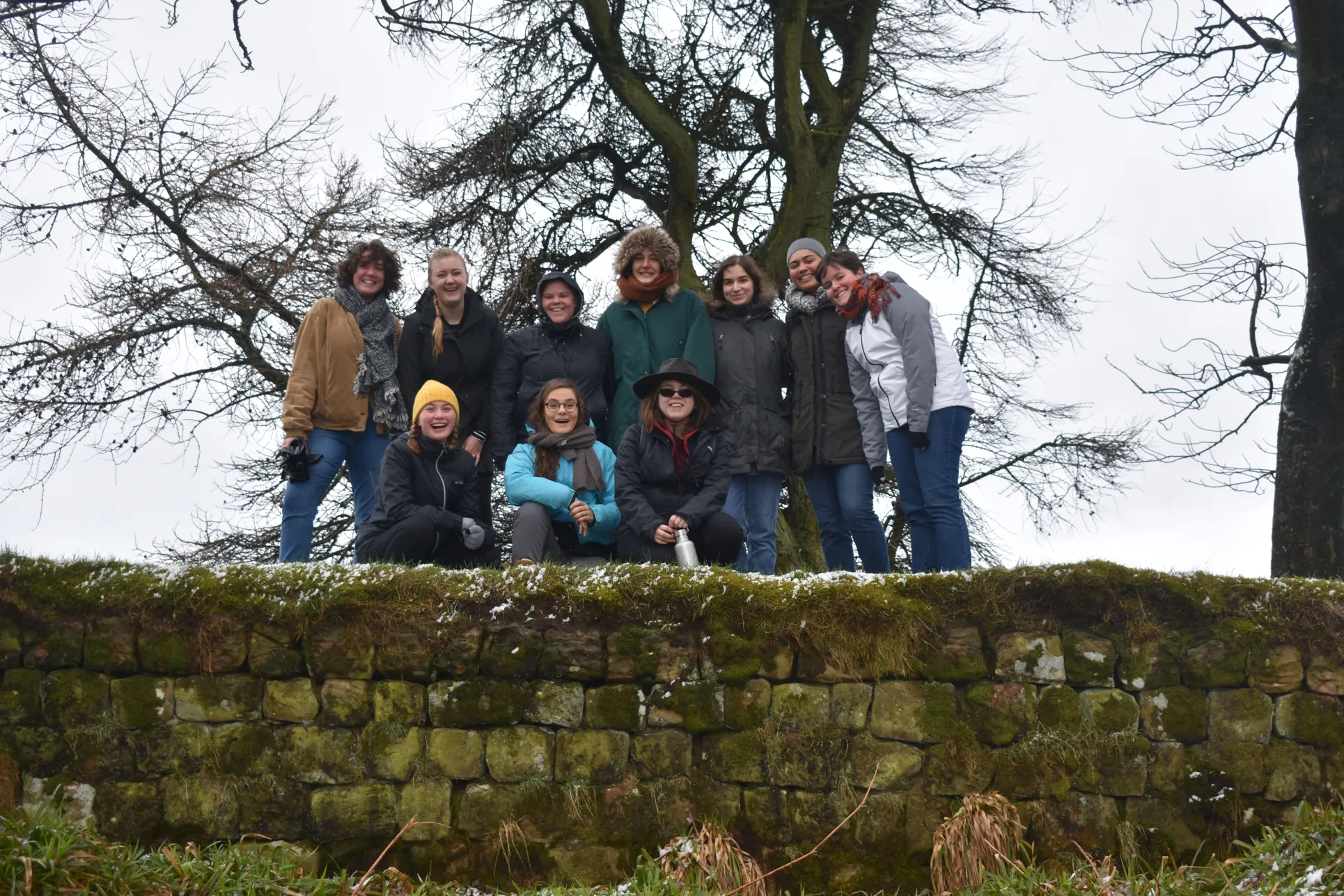 A group of Classical and Near Eastern Archaeology students stand on a green mossy portion of Hadrian's wall in winter