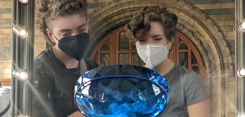 Two students observe a large blue gem through a museum case.