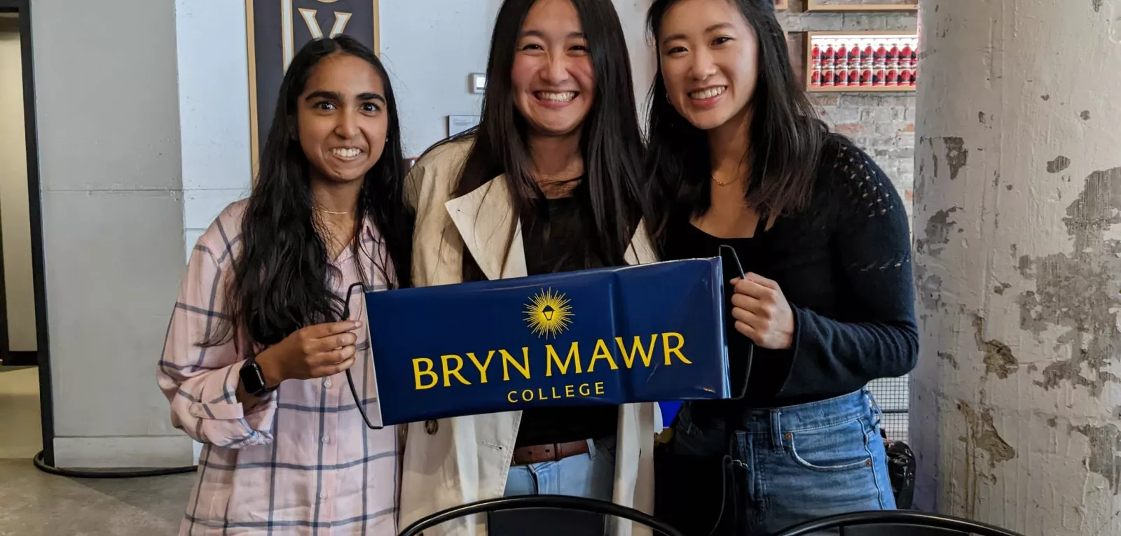 Three GOLD alums pose with a blue banner that says Bryn Mawr College.