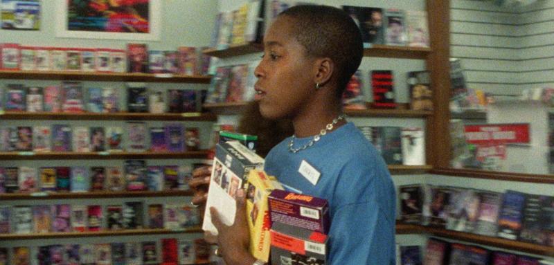 A woman walks through a video store holding a stack of VHS tapes