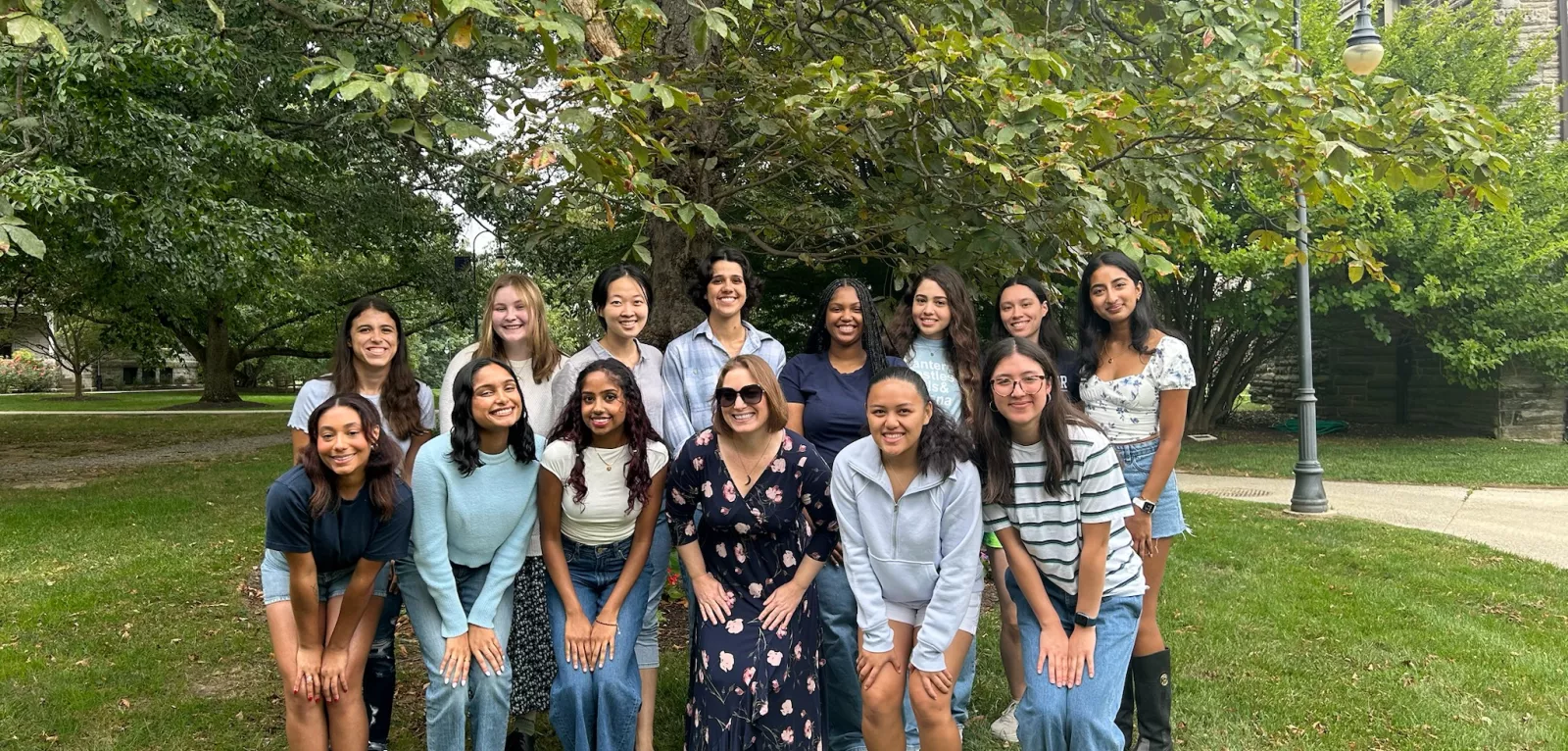 Group of people smiling and posed in front of a tree.