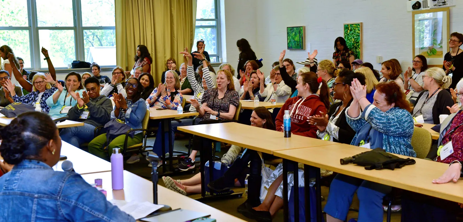 Alums sit in a classroom, cheering and laughing.