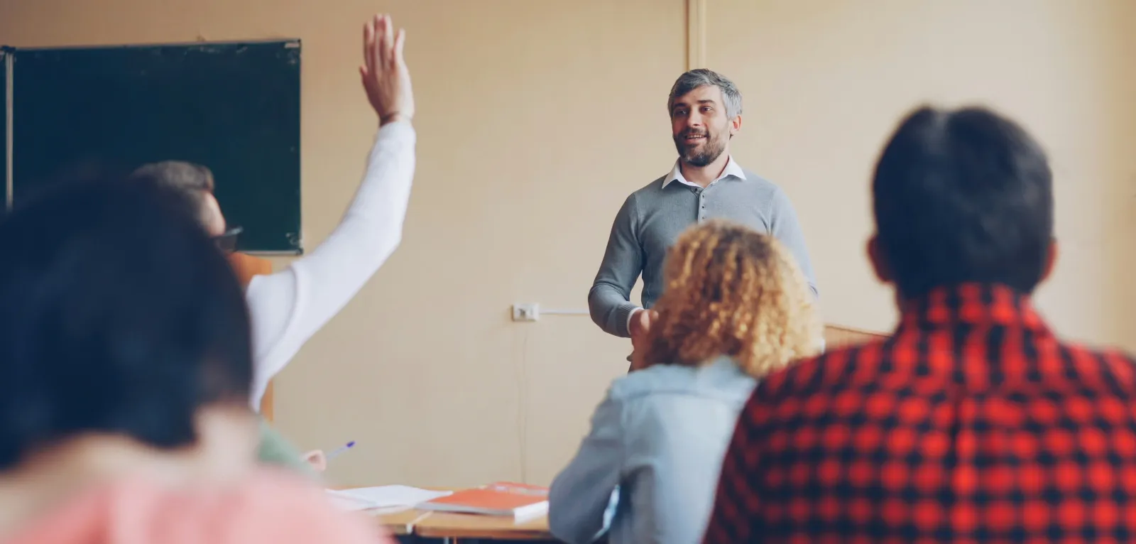 Man teaching class with student who is raising hand. 