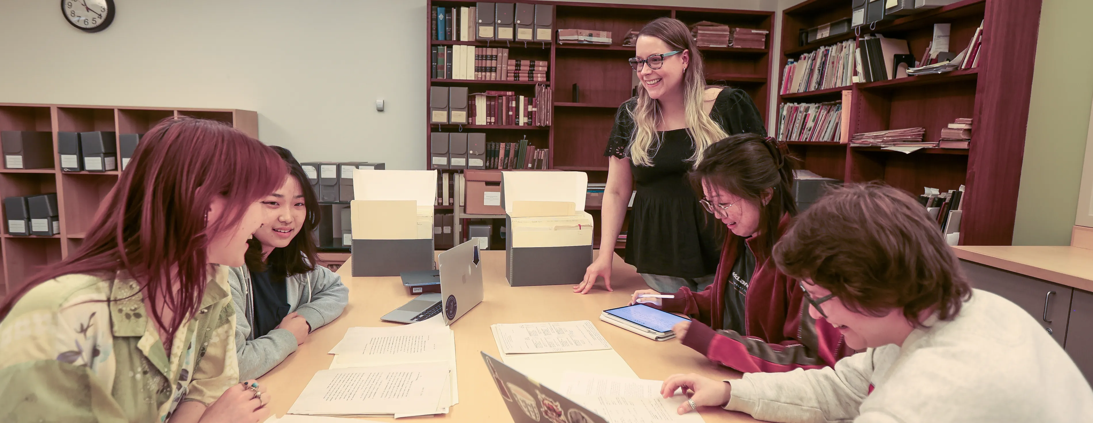 Four students doing archival research at a table while a staff member helps them. 