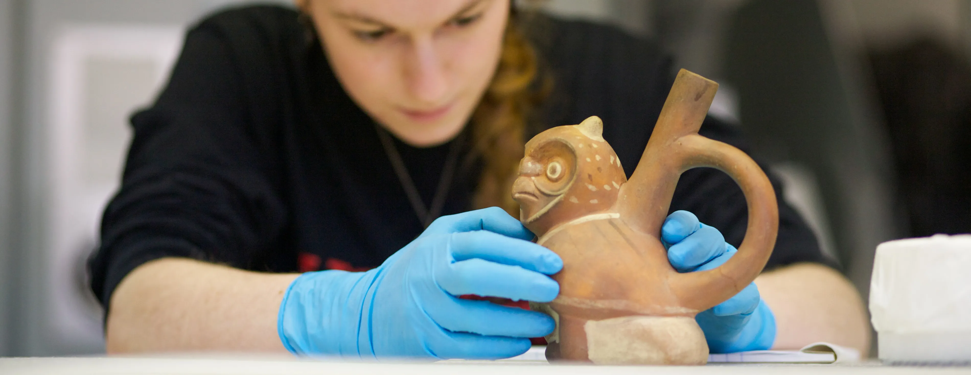 A Bryn Mawr College Art History student examines a clay vessel in the shape of an owl